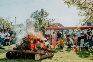 A lively community gathering enjoying a bonfire event outdoors on a sunny day.
