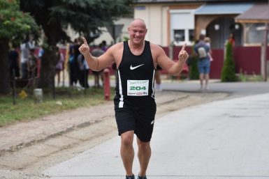 Joyful runner at a race finish line outdoors, raising arms in celebration.
